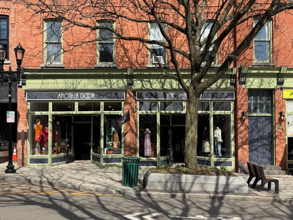 A shop called Another Door spans two shop fronts in a red brick building with a bare tree in front of it.