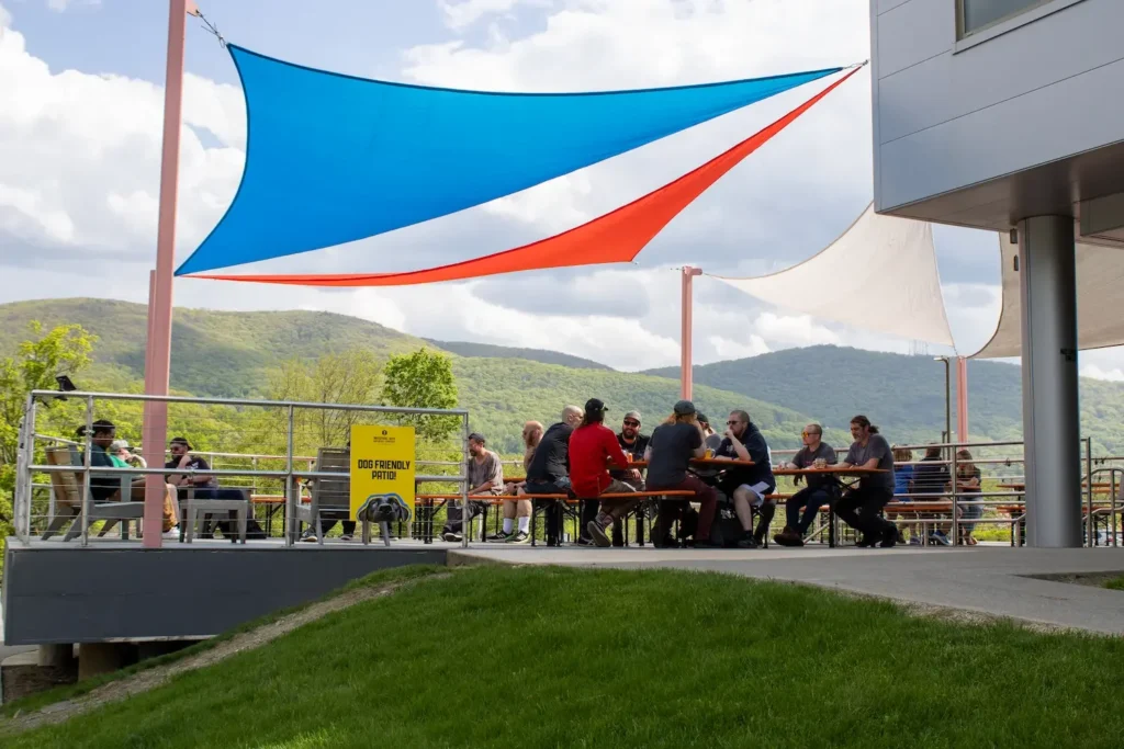 a patio in summertime filled with people sitting at tables, shielded from the sun by a blue, red, and white canopy.