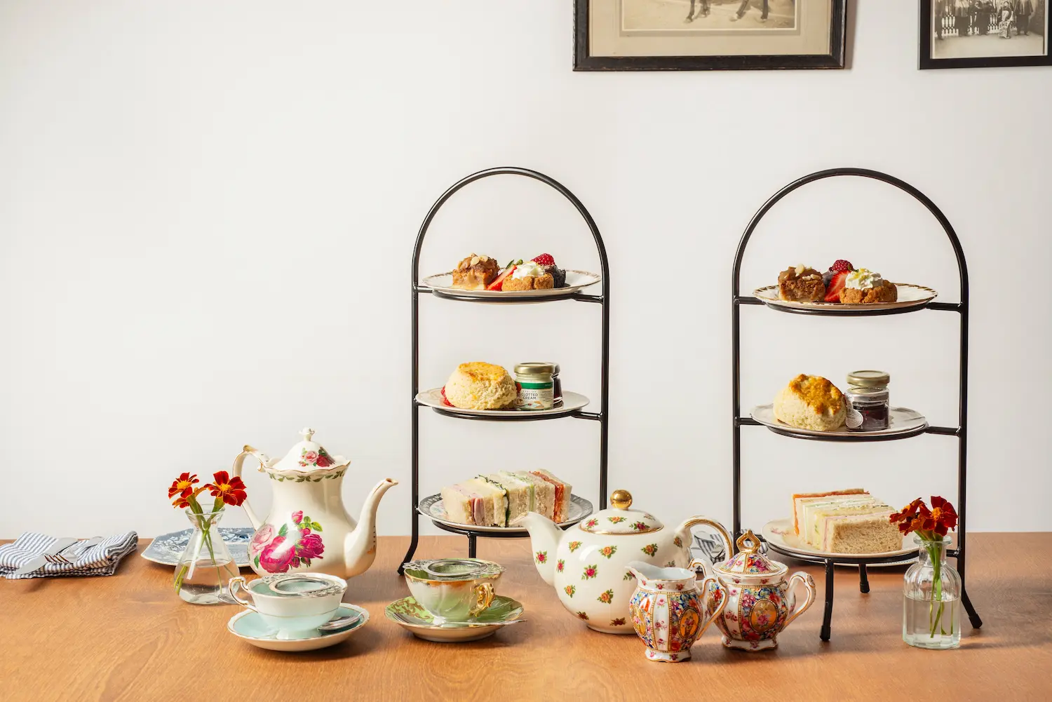 A spread of afternoon tea with scones, cakes, and small sandwiches with vintage pots of tea and crockery.
