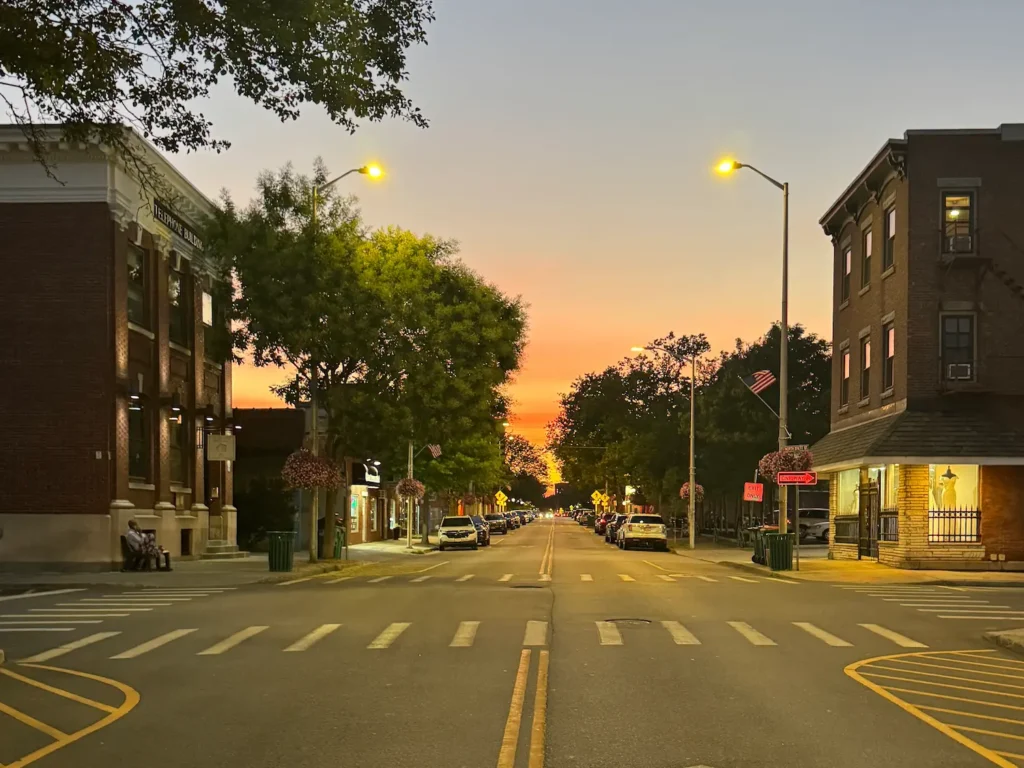 Beacon's Main Street at sunset with red brick buildings either side of the road. Crosswalks are in the foreground and sunset is in the background.