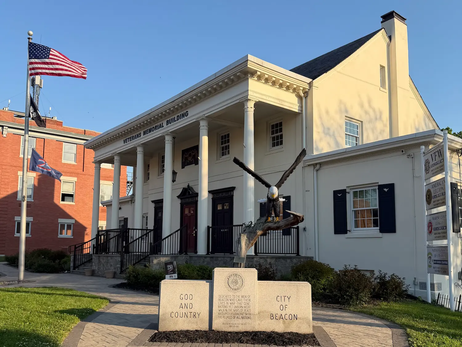 A cream colored Veterans Memorial Building in Beacon, with a n American flag flying high outside and a sculpture of an eagle.