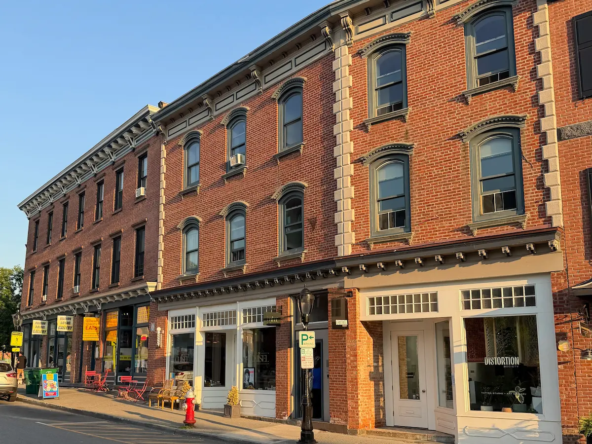 A line of red brick buildings with storefronts slope away from the camera with a blue sky in the backgroud.