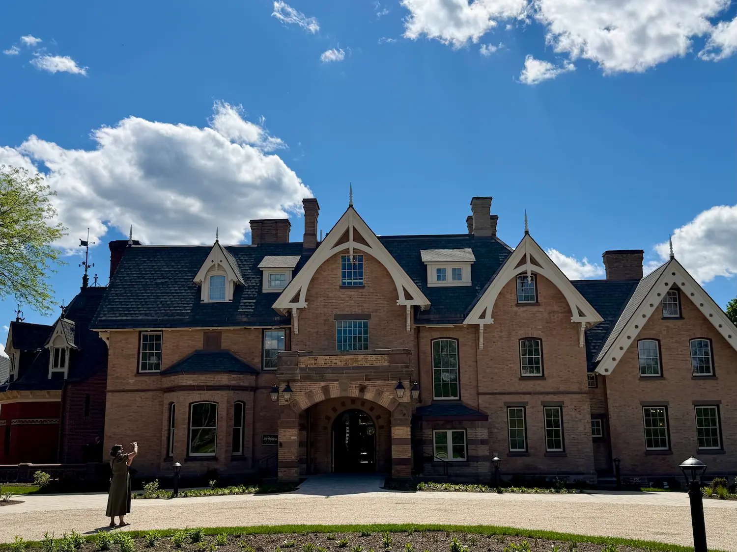 A beautiful victorian gothic mansion with a blue sky in the ground and a woman taking a photo of the building.