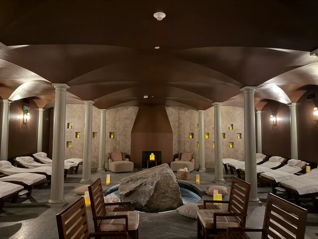 A large spa room with beds and candles in a darkly lit room and white columns and arched ceilings.