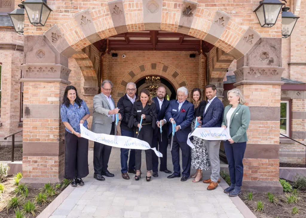 A group of VIPs cut a ribbon with large blue scissors to celebrate the opening of Mirbeau Beacon Inn & Spa