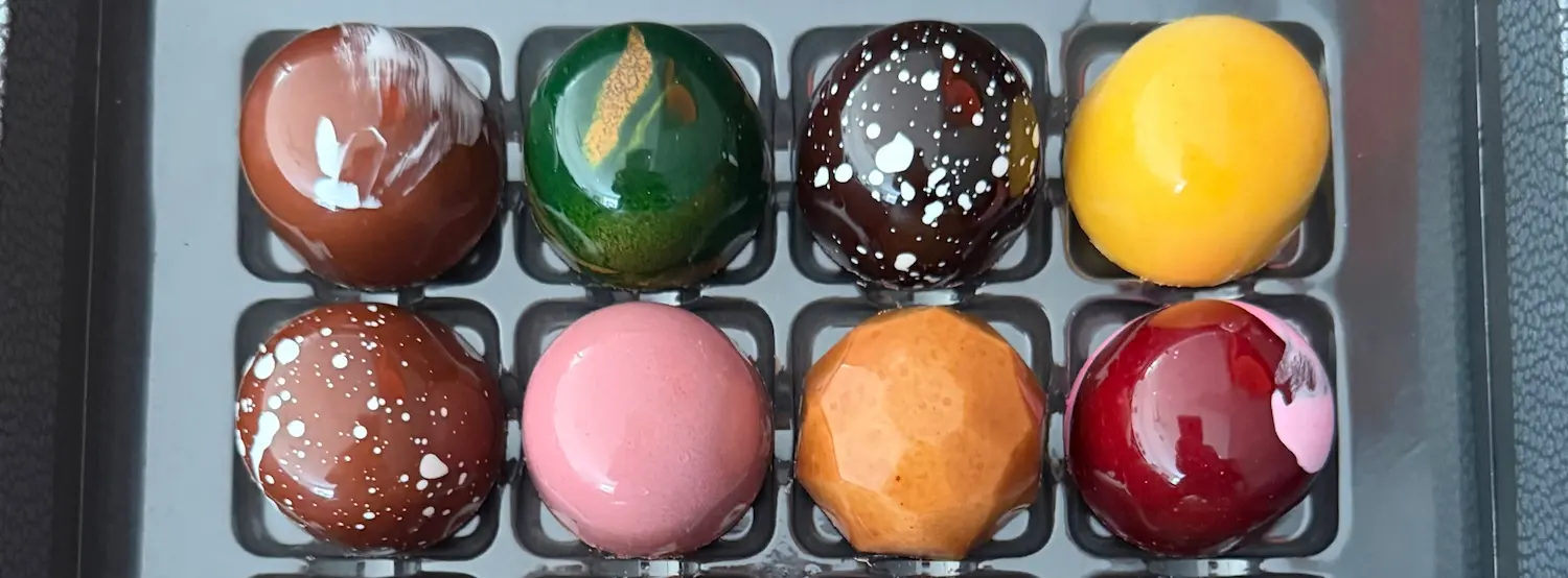 A tray of eight multi-colored chocolate bon bons.