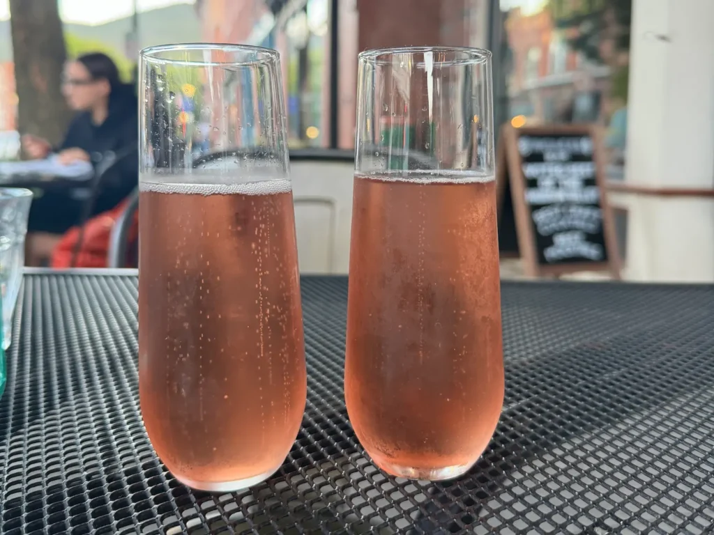 two chilled glasses of sparkling rose wine on a metal table with a person sitting outside in the background.
