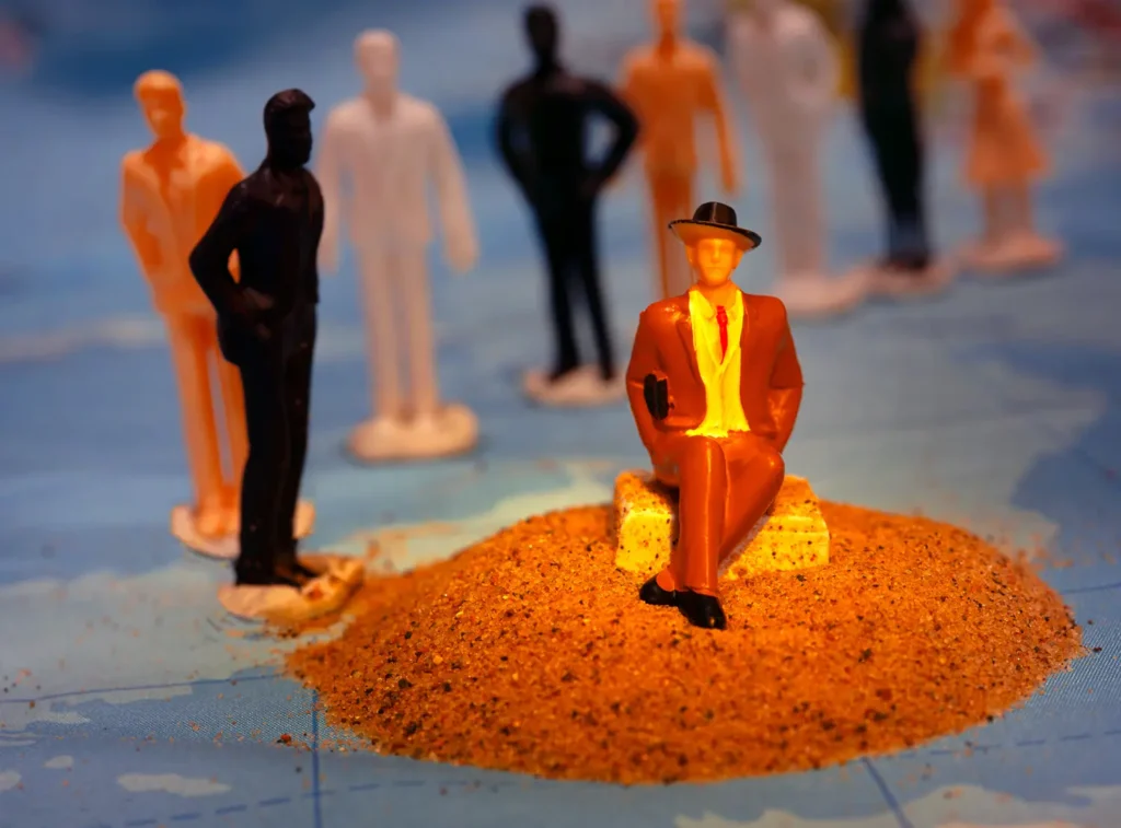 An artwork with miniature figures in orange and black. The main figure at the front of the image stands out for wearing a black hat and bright orange suit.