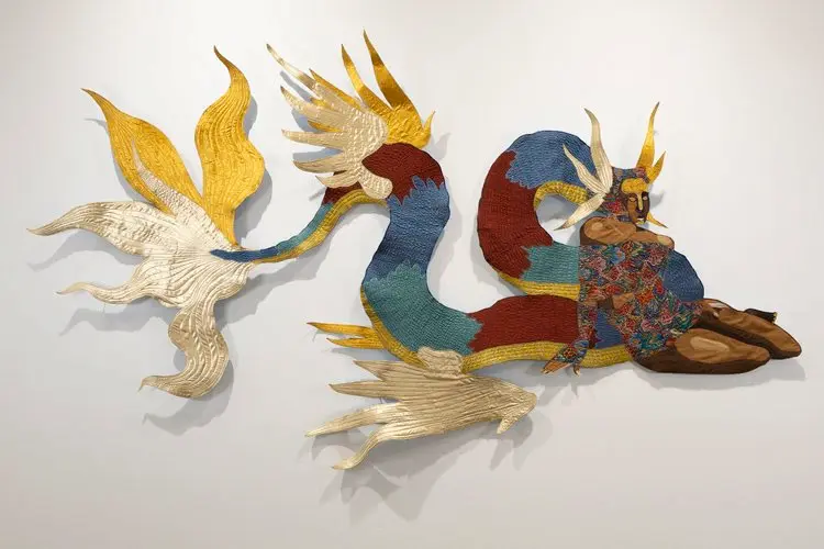 Colorful patchwork quilt art on a white wall in the shape of a snake or dragon.